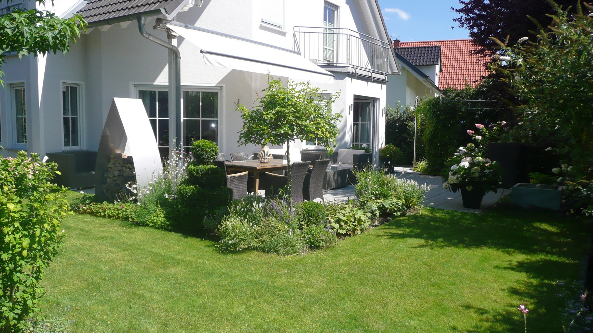 Garten nach Neugestaltung in klassischem Design, Rasenfläche und bepflanzte Beete an der möblierten Terrasse.