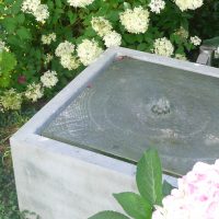 Grauer Quellstein als Wasserspiel im Hortensienbeet.