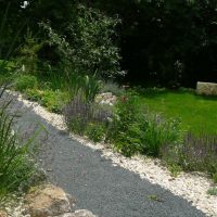 Geschotterter Gartenweg an Beet aus weißem Kiesel mit Bepflanzung.