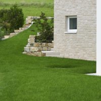 Neues Gartendesign für Hanglage mit Natursteinmauer abgefangen, große Rasenfläche und Beetemit blühenden Stauden und Sträuchern.