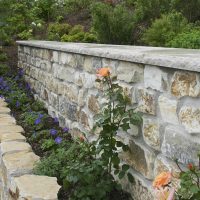 Abfangen der Hanglage mit gemauerten Naturstein als neues Gartendesign für Beete mit Rosen und blühenden Stauden in unterschiedlicher Höhe.