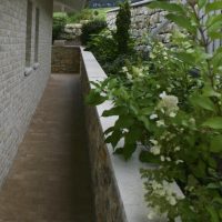 Neugestaltung des Gartens mit Gartenweg, Stützmauer aus Naturstein und Hochbeet mit Stauden und blühenden Sträuchern.