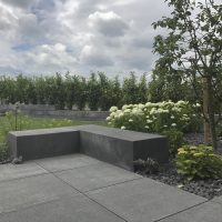 Modernes Gartendesign neu geplant und gestaltet - Bodenplatten und eine Steinbank aus Blocksteinen in Betonoptik. Das Schotterbeet, bepflanzt mit Fetthenne und weißen Hortensien, Ziergräser und Obstbaum.