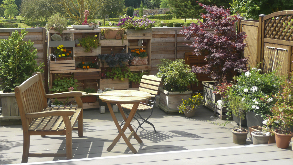 Möblierte Holz-Terrasse mit vertikalem Garten, unterschiedliche Kübelplanzen.