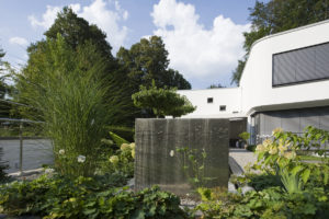 Gartenplanung eines modernen Gartens in Bad Homburg - Der modernen Architektur im Design angepasst, Wasserfall / Wasserwand aus Edelstahl, das Staudenbeet bepflanzt mit Chinagras, weißen Anemonen und Hortensien.