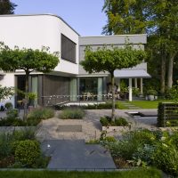 Gartenplanung eines modernen Gartens in Bad Homburg - Der Garten ist angepasst an die moderne Architektur. Große Trittplatten, Kieswege und Inselbepflanzung mit Edelstahlkante, bepflanzt mit Eiben, Lavendel. Dachplatanen erzeugen eine weitere Ebene des Gartens.