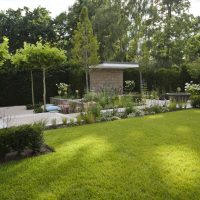 Modernes Gartenhaus mit kleiner Terrasse, grosse Rasenfläche mit Blumenbeeten und niedriger Hecke umrandet.