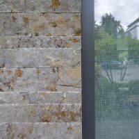 Wandgestaltung aus bunten Naturstein-Klinker in Rosttönen. Im Fenster Spiegelbild des Vorgartens