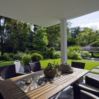 Überdachte Terrasse modern möbliert, mit Blick auf den neu geplanten und gestalteten Garten in modernem Design. Rasenfläche mit großen Rinnit Trittplatten zum Wasserbecken mit Edelstahl-Umrandung.