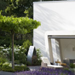 Gartenplanung und umgestaltung des Gartens mit überdachter Terrasse in modernem Design, Pflanzinseln mit Lavendel im Kiesweg, Schirmplatane mit Edelstahlkante als Umrandung.