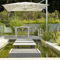 Planung und Gestaltung eines modernen Gartens in Hofheim - Wasserbecken mit Wasserwürfel und Trittplatten in Betonoptik, Terrasse modern möbliert und dekoriert.