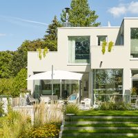 Planung und Gestaltung eines modernen Gartens in Hofheim - Gebäudeansicht mit Terrasse, Rasenstufen mit Edelstahlkante und Staudenbeet