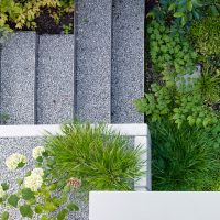 Planung und Gestaltung eines modernen Gartens in Hofheim - Stufen, geformt aus Edelstahlkanten, aufgefüllt mit Kies. Bepflanzung des Schattengartens mit Chinaschilf, Kirschloorbeer und unterschiedliche Bodendecker.