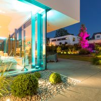 Beleuchteter Garten bei Nacht, möblierte Terrasse und bepflanztes Schotterbeet. Gartengestaltung der modernen Architektur des Hauses angepasst.