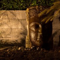 Gartendekoration Buddha-Kopf beleuchtet, in Schotterbeet, bepflanzt mit Ziergras.