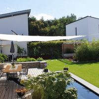 Blick auf einen modernen Garten, mit Terrasse unter Sonnensegel, Senkgarten mit Sitzplatz und Wasserbecken.