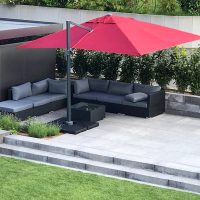 Großer, roter Sonnenschirm über hochwertige Gartenmöbel auf erhöhter Sitzfläche aus grauem Stein. Pflanzinsel mit Lavendel und Ziergras, sowie Gartendekoration